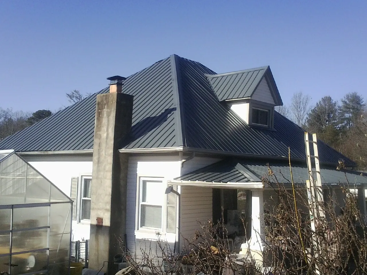 Dark blue standing seam metal roof on a white farmhouse with dormer — Slate & Tile Roof Repair by Roofing Brothers in Staley