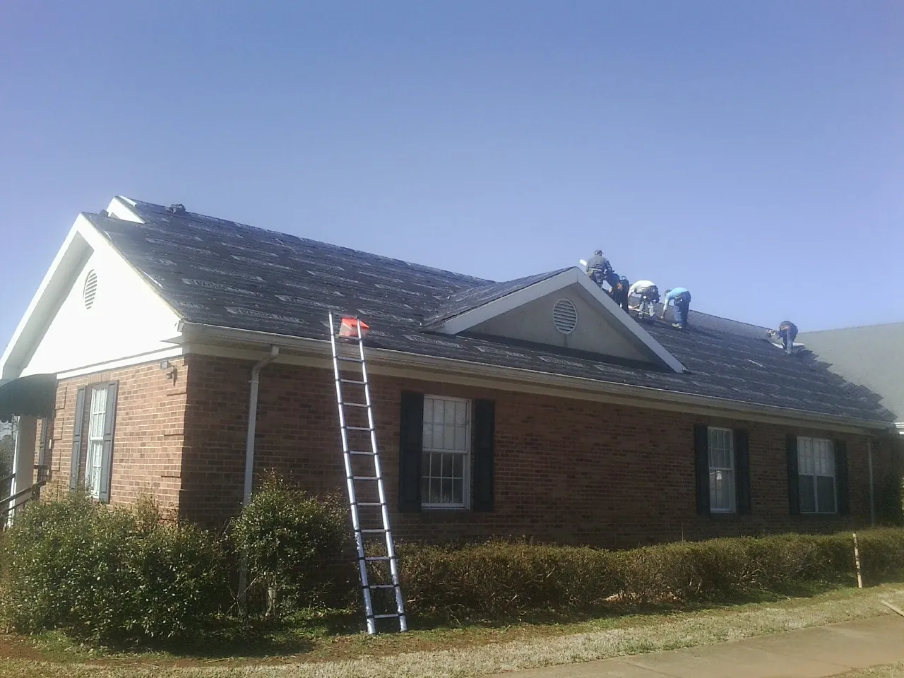 Crew tearing shingles off a brick ranch roof with a ladder set — Emergency Roof Repair work by our crew in Staley