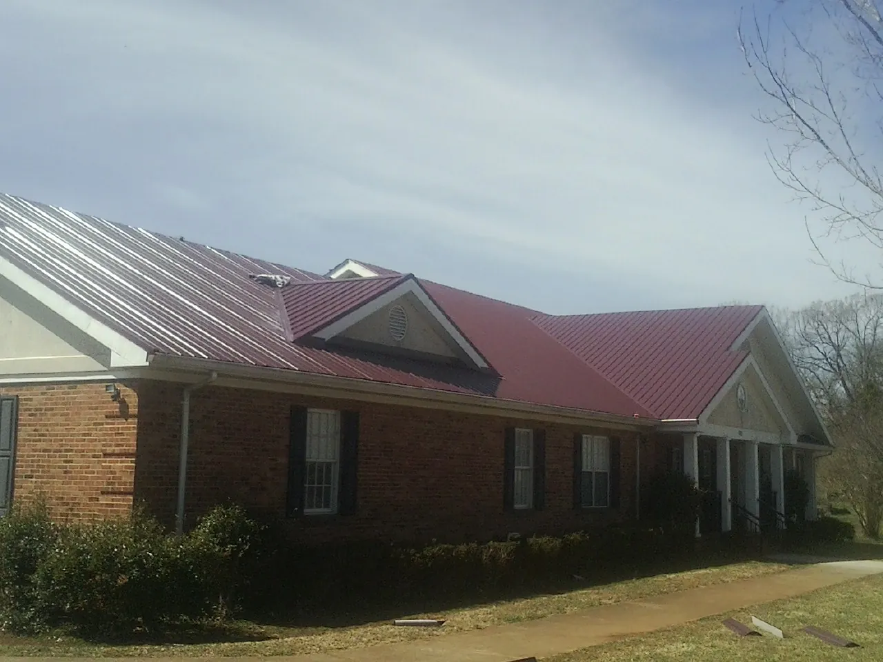 Red metal roof with gabled entries on a long brick building, from a Hail Damage Roof Repair job in Staley