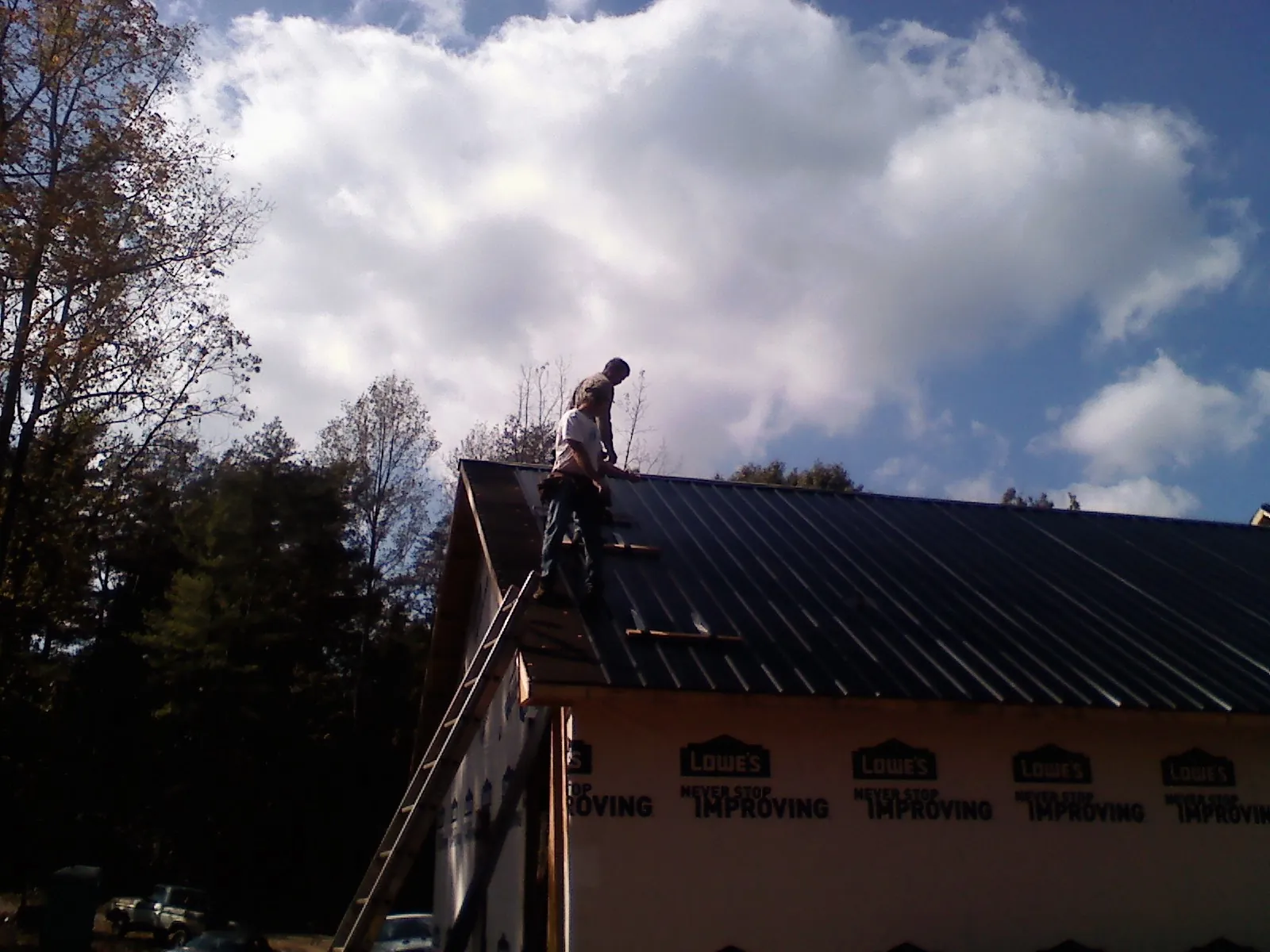 Roofer fastening dark metal panels high against a cloudy sky, from a Roof Inspection job in Staley
