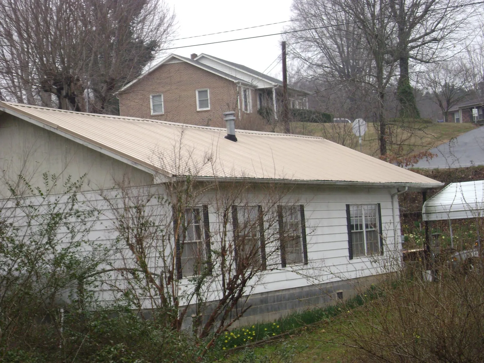 Tan metal roof on a white sided house set into a hillside — Commercial Roofing by Roofing Brothers in Staley